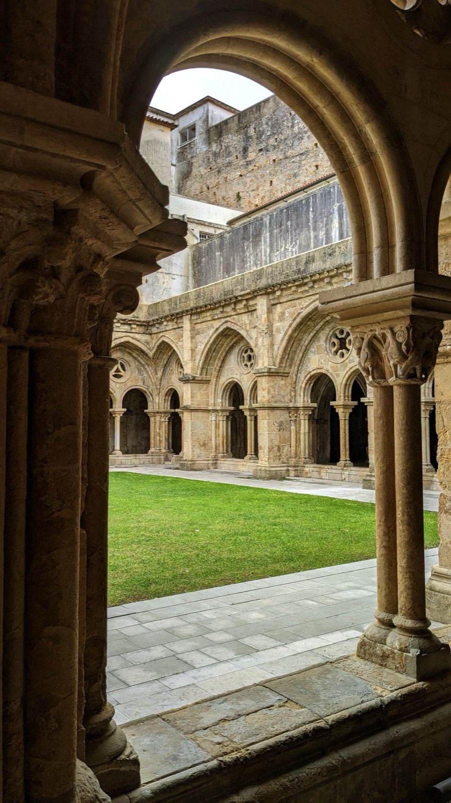 Cloister arches framing a green courtyard in Coimbra