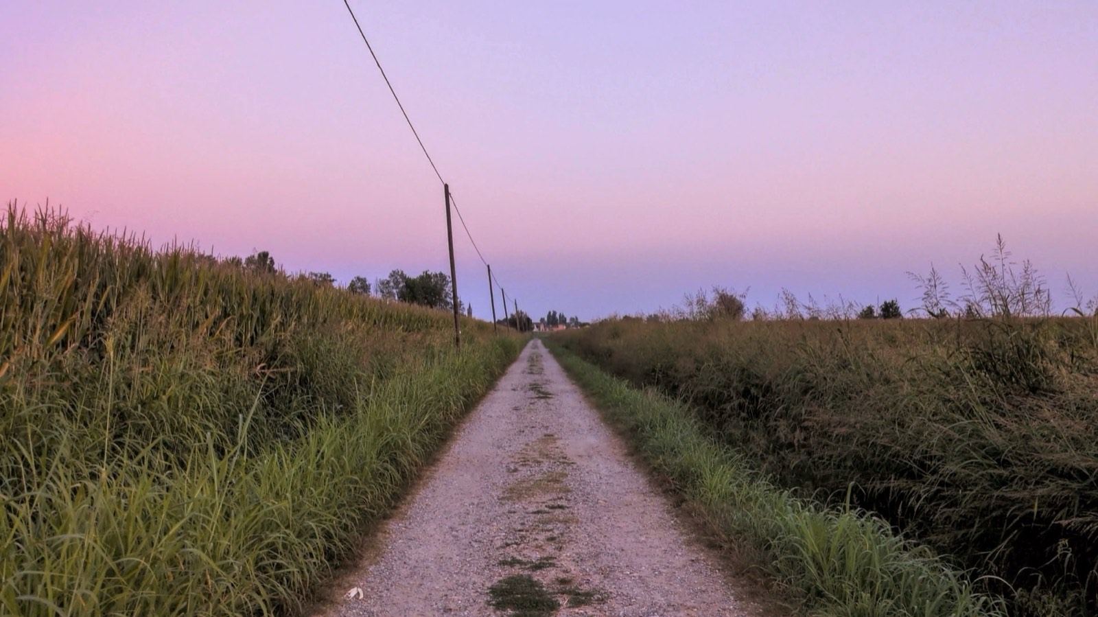 Gravel path between fields at dusk under a pink sky, by the Adda